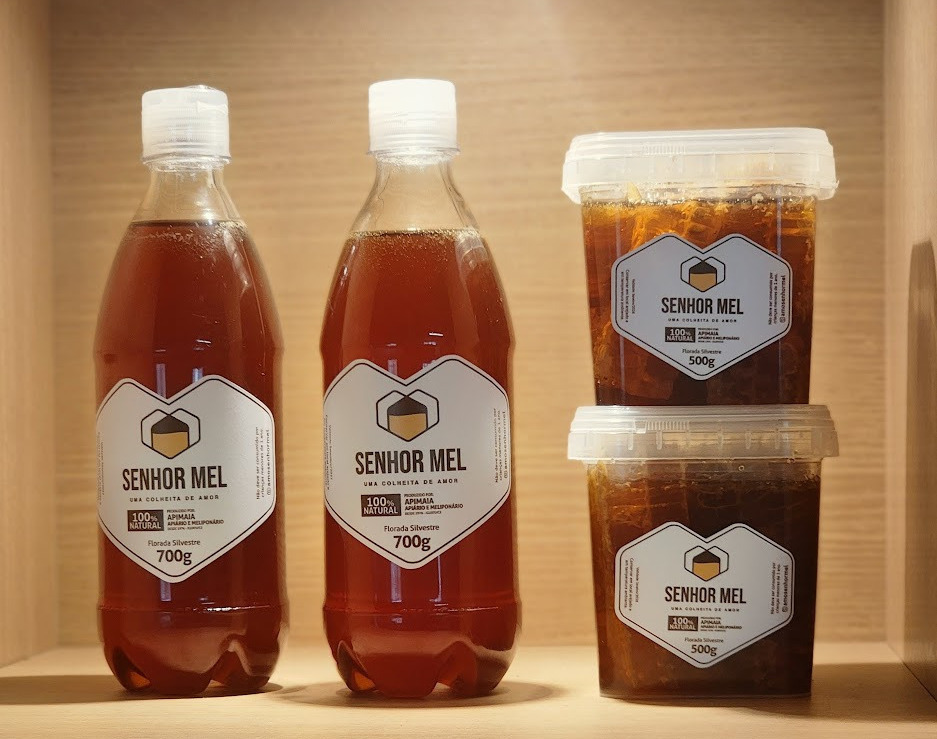 Garrafas de 700 g de mel Senhor Mel ao lado dos potes de 500 g de favo e mel